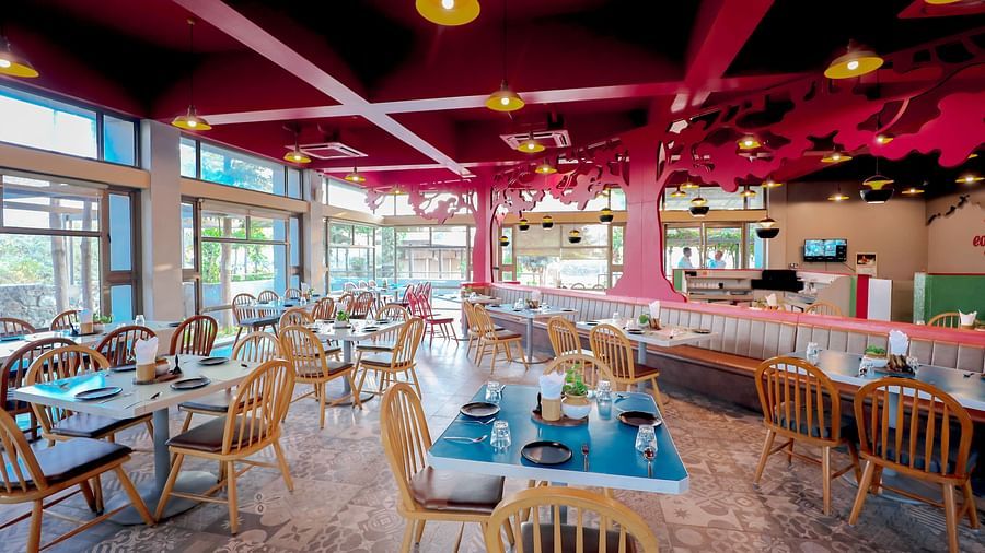 An image of a restaurant featuring chairs, tables, tree cutouts on top with ceiling lights - Pride Resort Ambaji